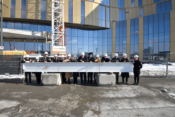 A group of people standing alongside President Lenton at the Markham Campus ‘topping-off ceremony’ behind a construction beam.”