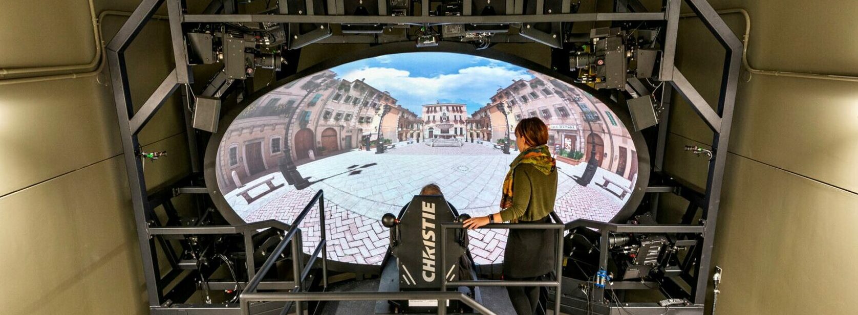 Two people watch a projection of a city on a digital dome.